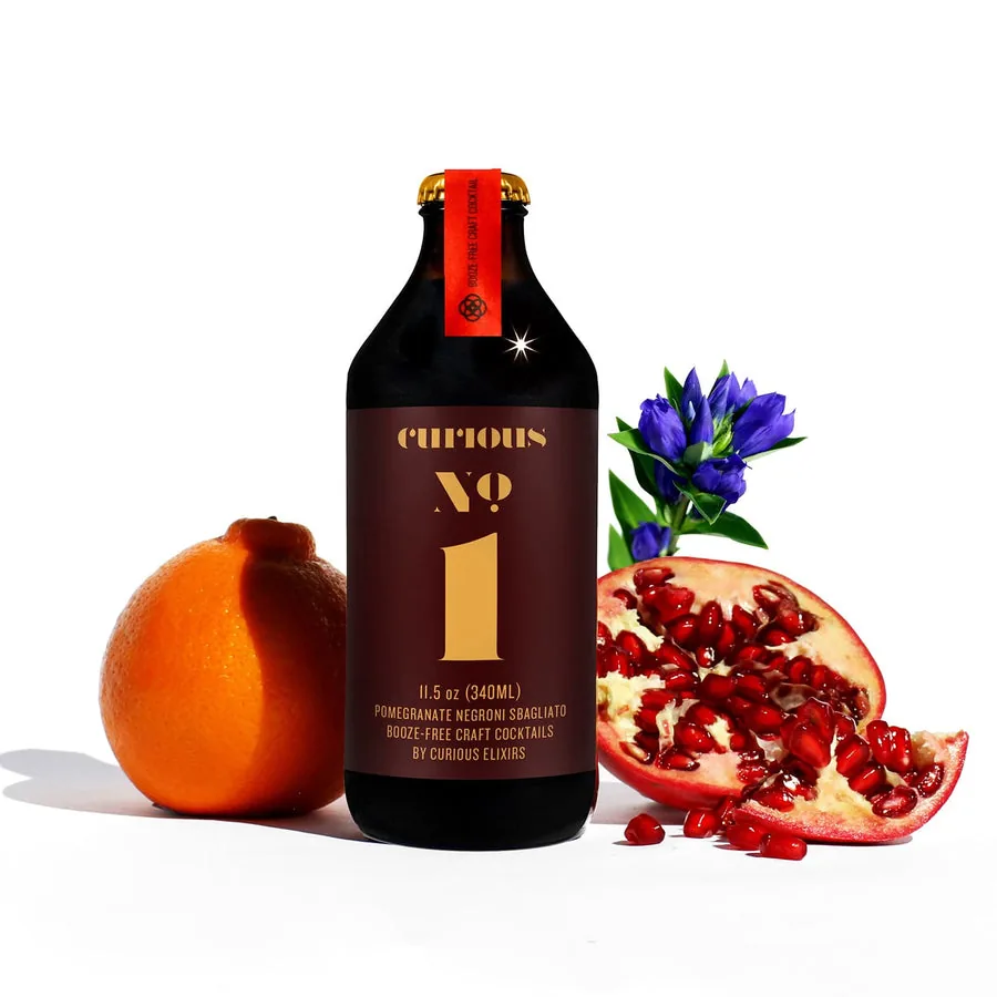 Curious No. 1, a non-alcoholic Pomegranate Negroni Sbagliato, beside fresh pomegranate and bitter orange.