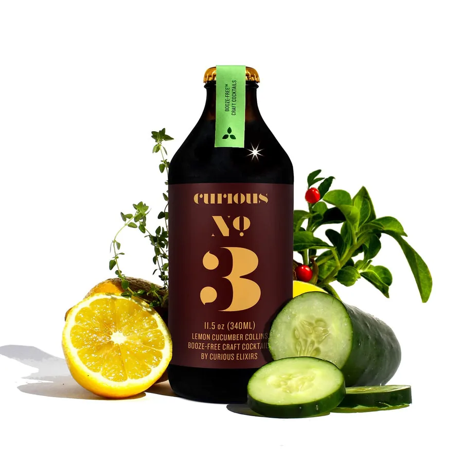 Curious No. 3, a non-alcoholic Juniper Cucumber Collins, beside fresh cucumber, lemon, and juniper.